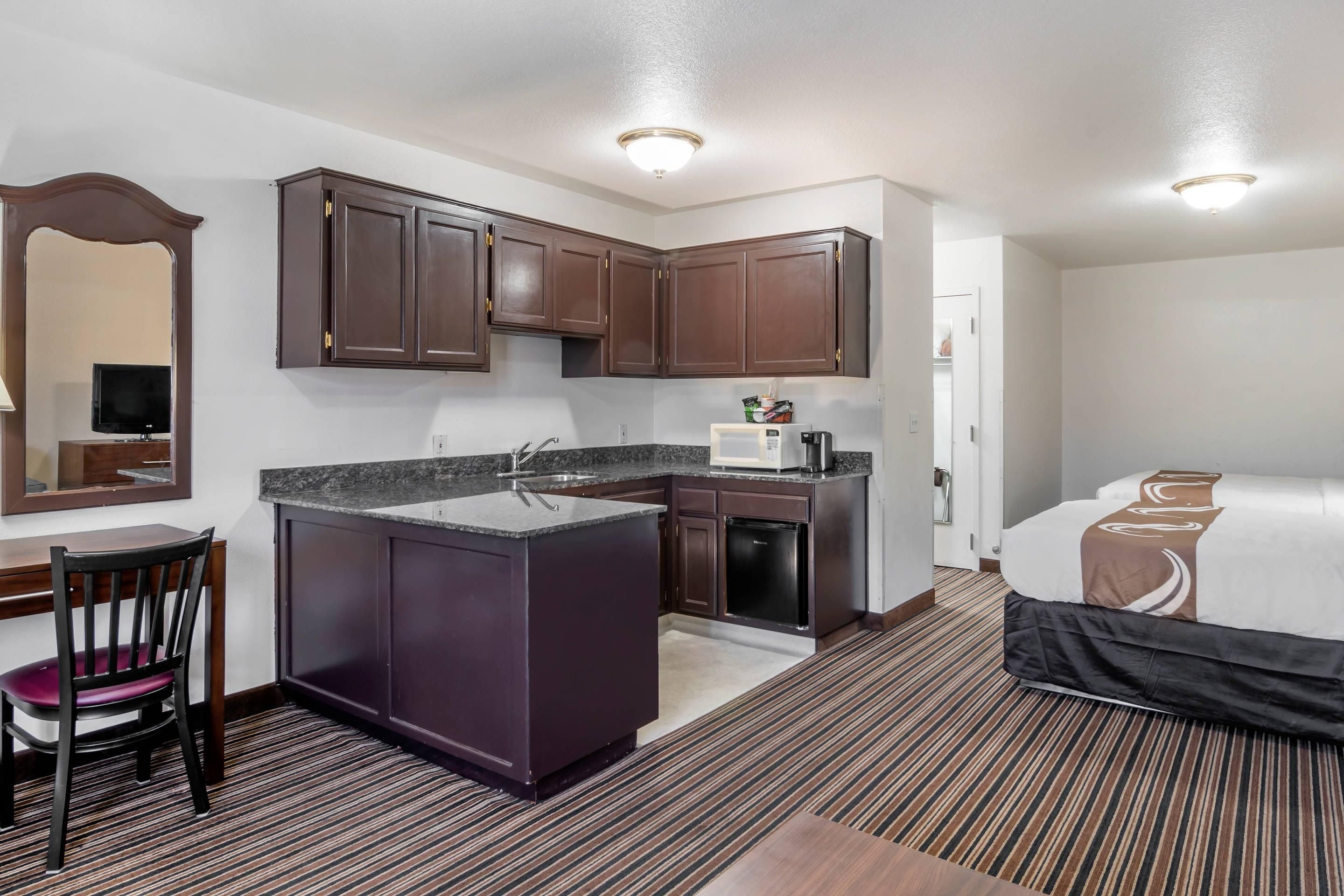 A hotel room with a kitchenette, a bed, a desk, and a chair.
