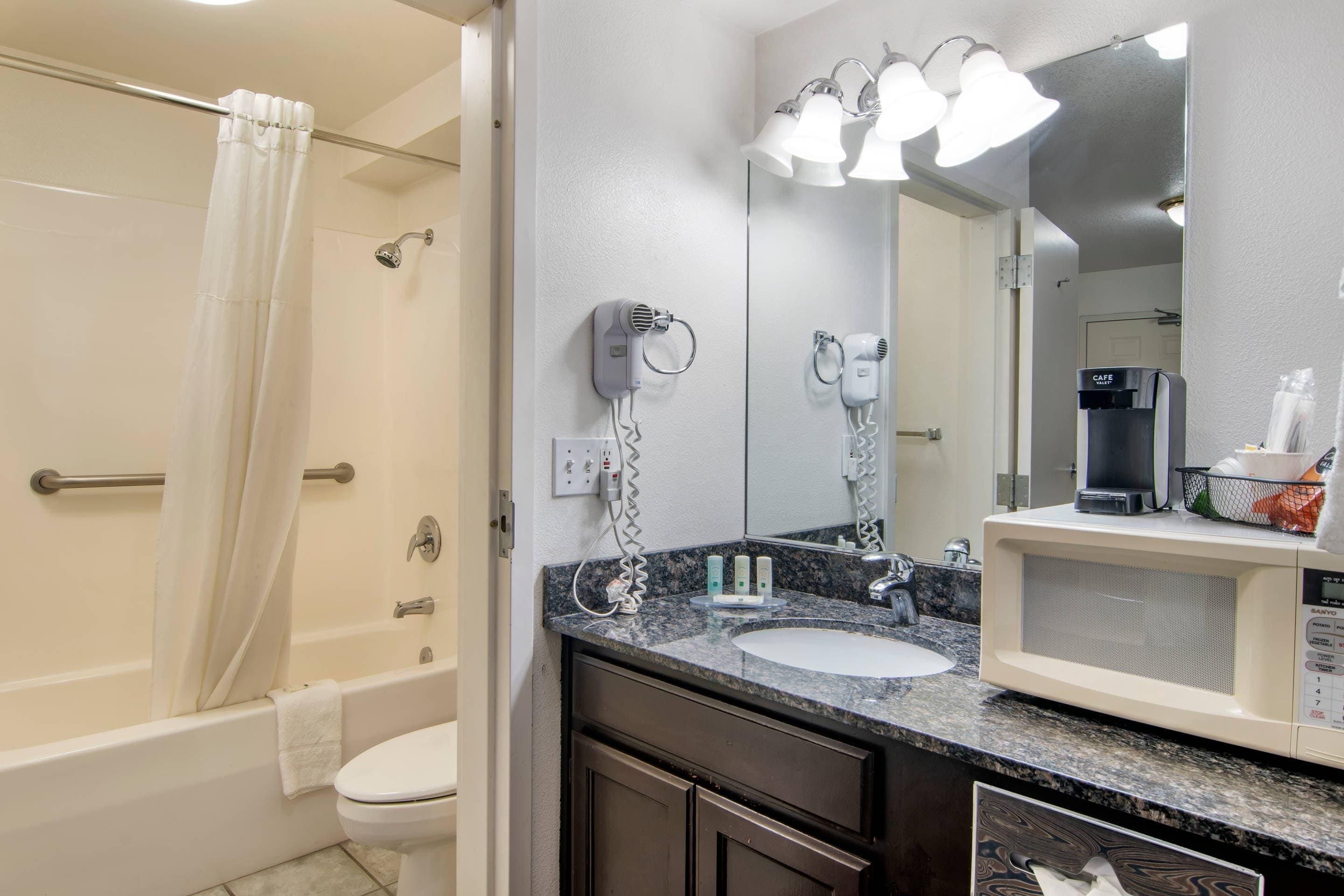 A bathroom with a shower, toilet, sink, and a mirror with lights.