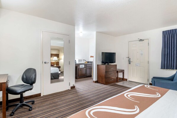 Quarto de hotel com cama, escrivaninha com cadeira, televisão, cómoda e banheiro visível através de uma porta aberta.