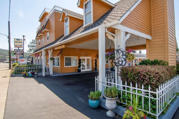 Classic motel with a two-story design, featuring a front porch and a fenced yard with potted plants.