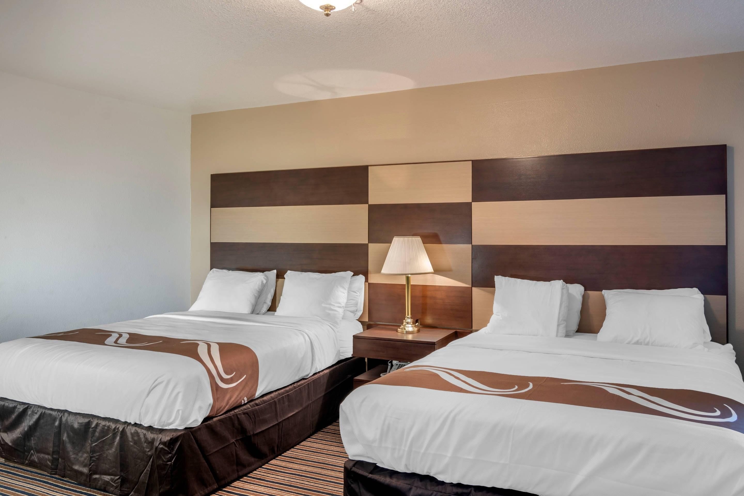 A hotel room with two beds, a headboard with a checkered pattern, a bedside lamp, and a striped carpet.