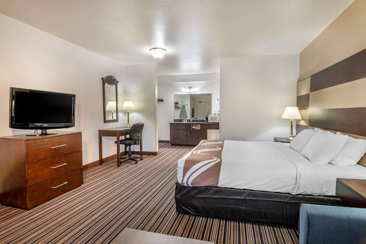 A hotel room with a bed, a desk, a television, a dresser, and a mirror.