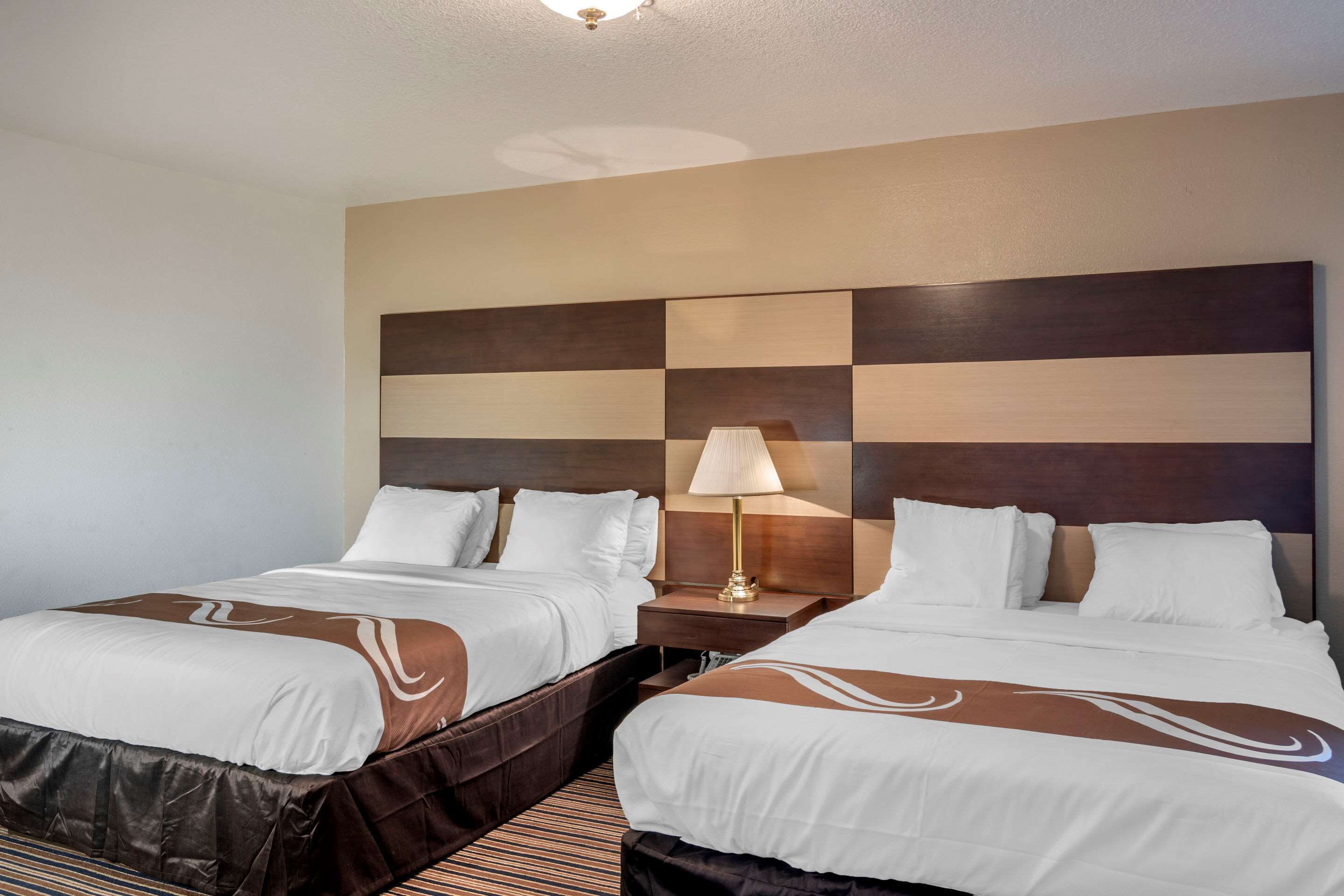 A hotel room with two beds, a large checkered headboard, and a bedside lamp.