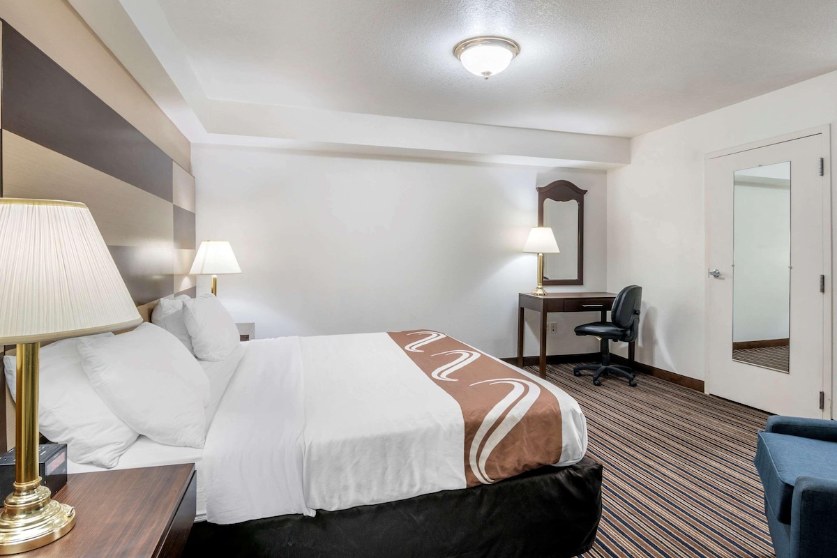 A hotel room with a bed, two bedside lamps, a desk with a chair, and a mirror.