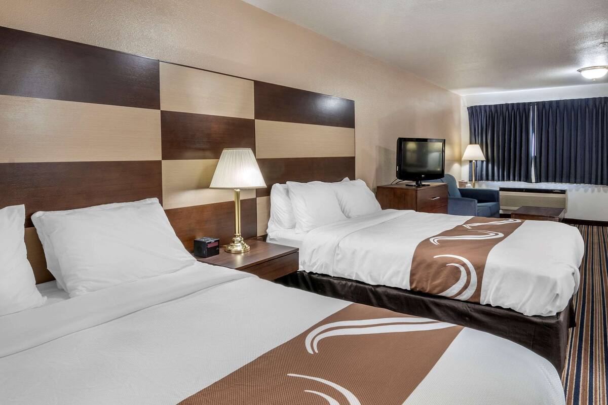 A hotel room with two beds, a television, a desk, and a window with curtains.