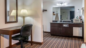 A hotel room with a desk, chair, two lamps, a large mirror, a kitchenette with a microwave, and a striped carpet. - Quality Inn Central Roseburg (Roseburg)