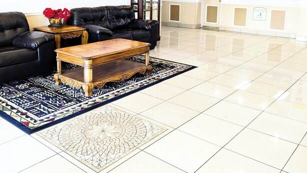 A lobby with a black leather sofa, a wooden coffee table, and a patterned rug. There is a reception desk in the background.