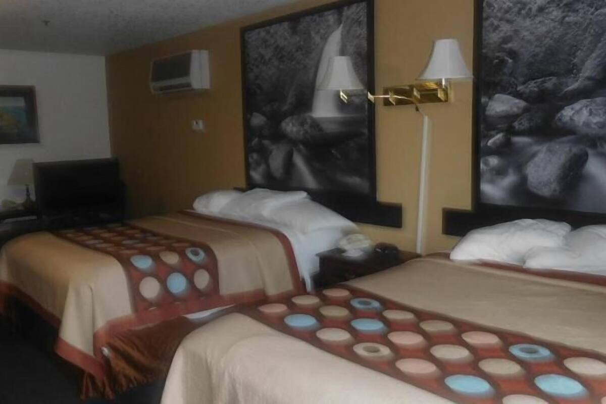 Een hotelkamer met twee bedden, een bureau met lamp en een schilderij aan de muur.