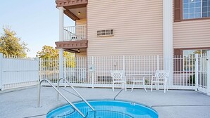 A swimming pool with a metal ladder, surrounded by a white fence and a building with a balcony.