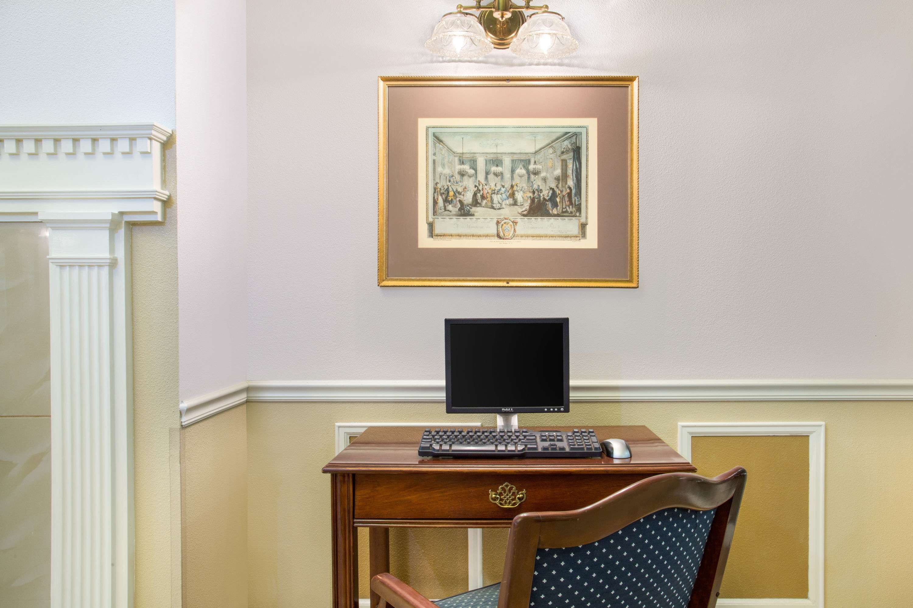 Ein Zimmer mit Schreibtisch, Computer, einem gerahmten Bild an der Wand und einem Stuhl.