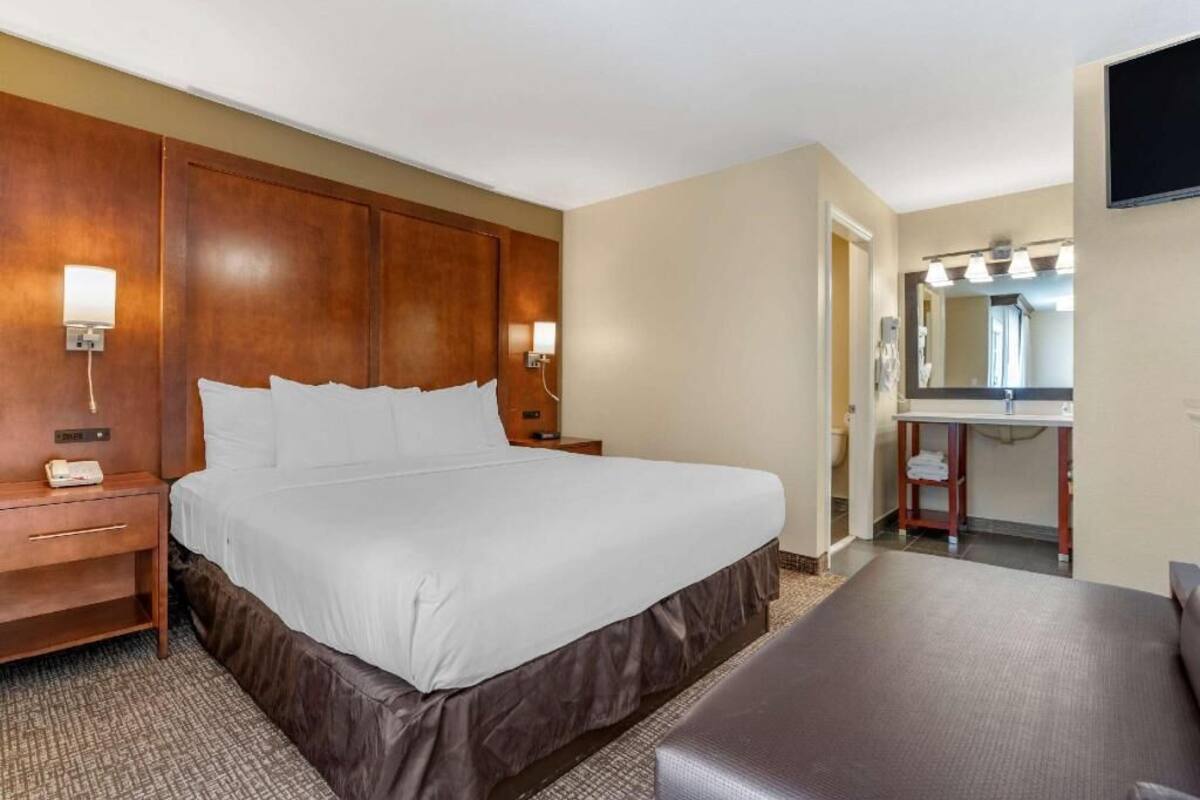 A hotel room with a large bed, bedside tables, a desk, a mirror, and a TV.