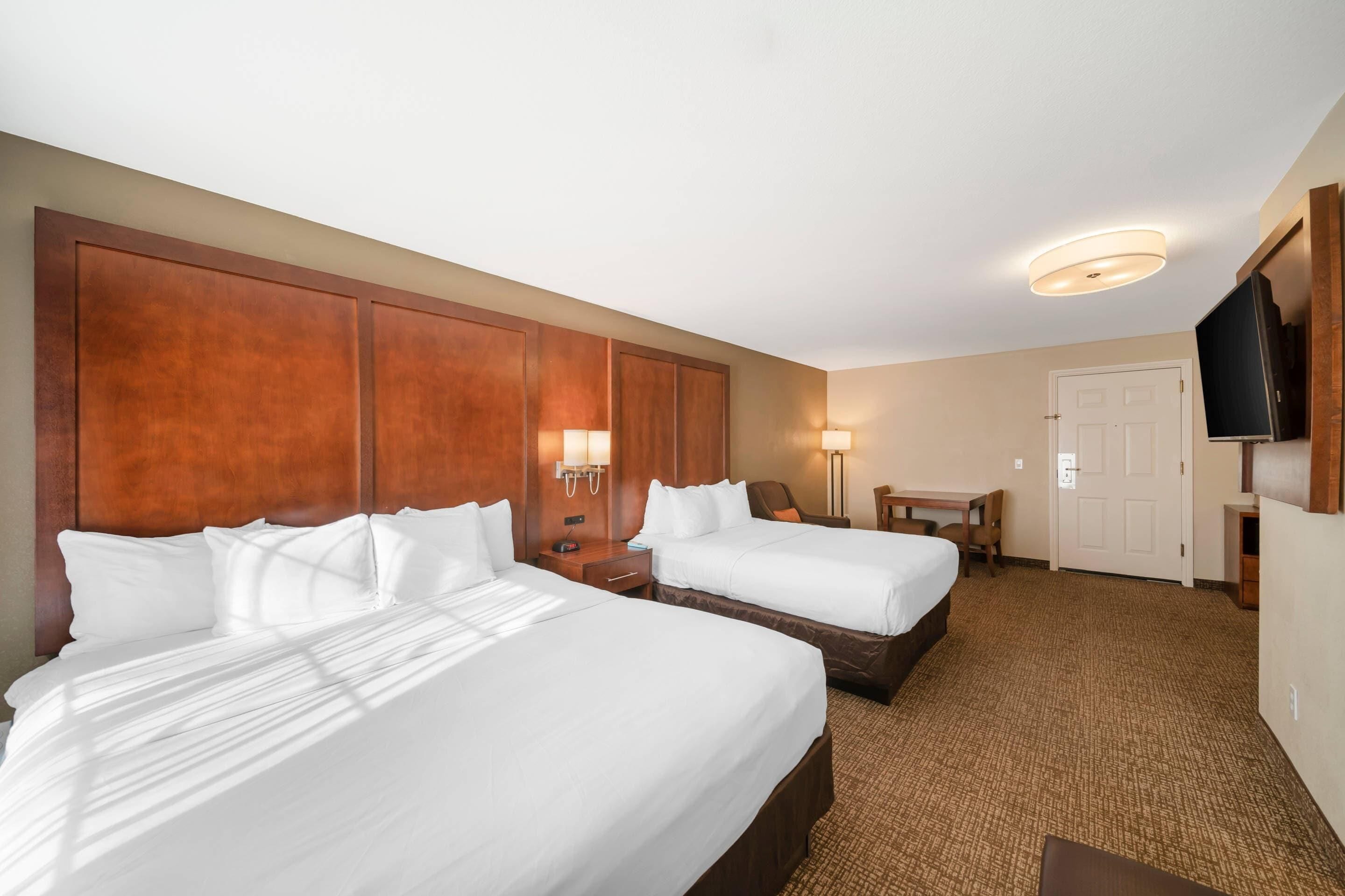 Habitación de hotel con dos camas, un escritorio, una silla, un televisor y una puerta.