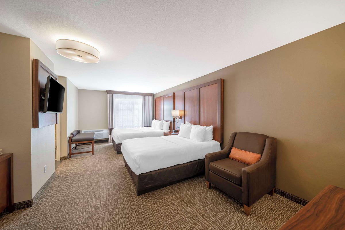 A hotel room with two beds, a TV, a desk, and a chair.