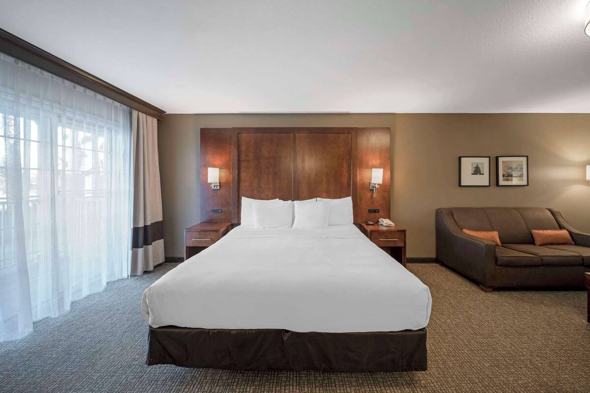 A hotel room with a large bed, a sofa, two bedside tables, and a window with curtains.