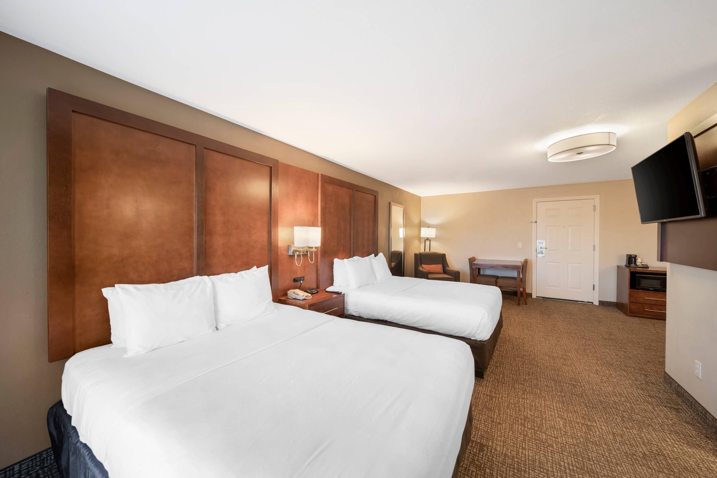 Habitación de hotel con dos camas, un escritorio, una silla, un televisor y una puerta.