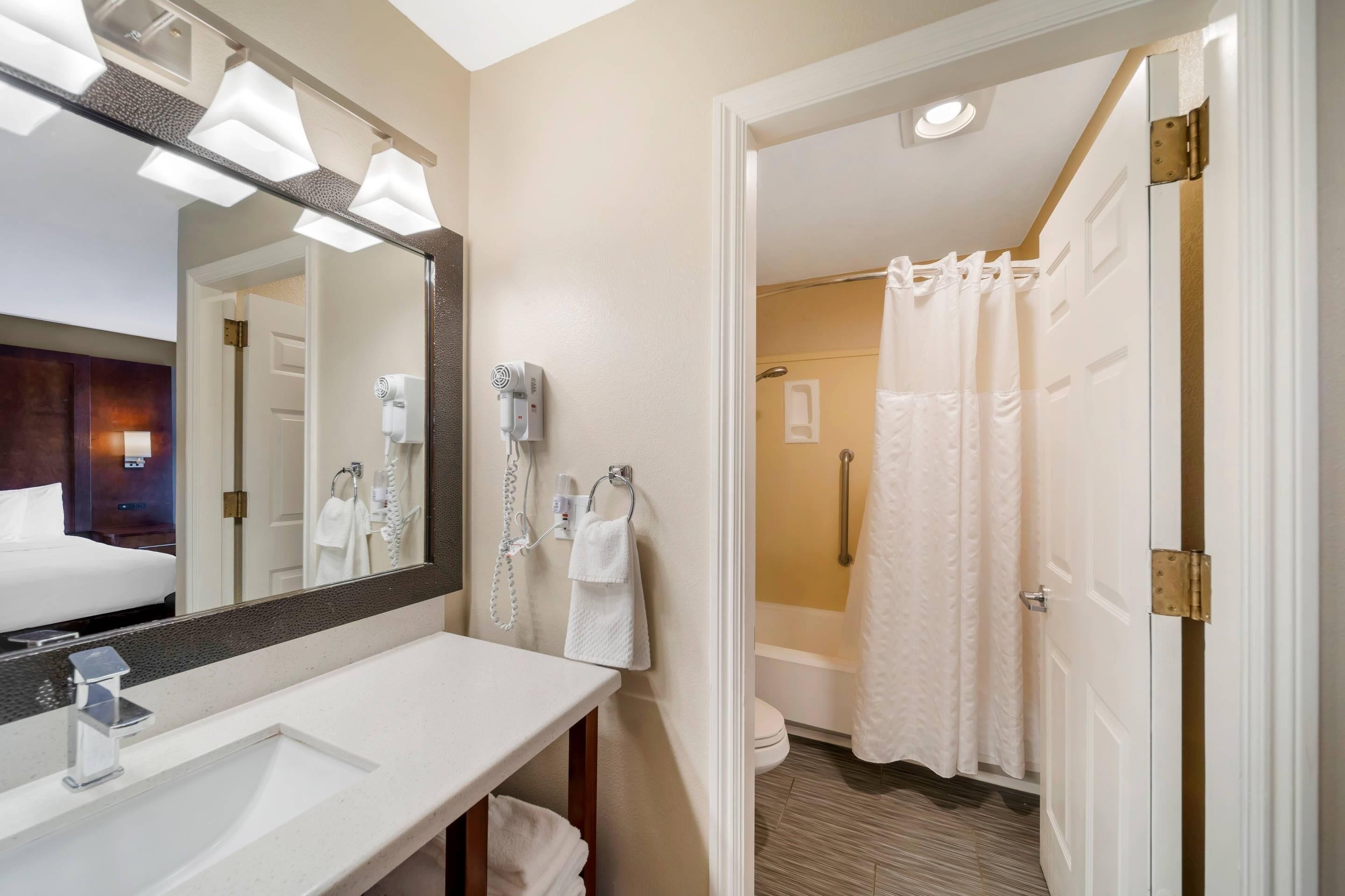 A hotel bathroom with a large mirror, a sink, a towel rack, and a shower area.