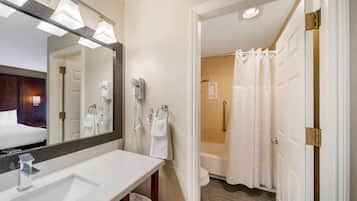 A hotel bathroom with a large mirror, a sink, a towel rack, and a shower area.