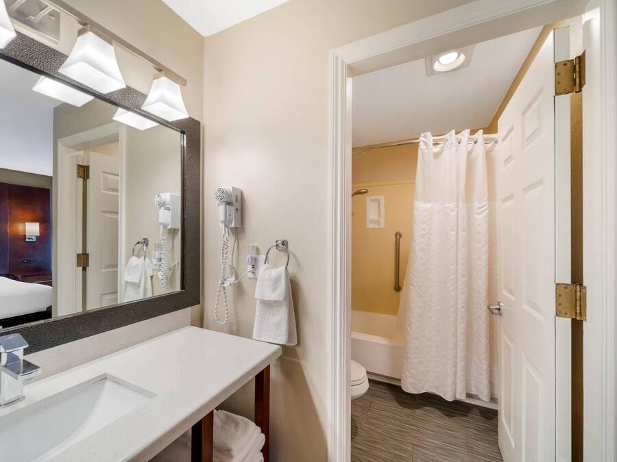 A hotel bathroom with a large mirror, a sink, a towel rack, and a shower area.