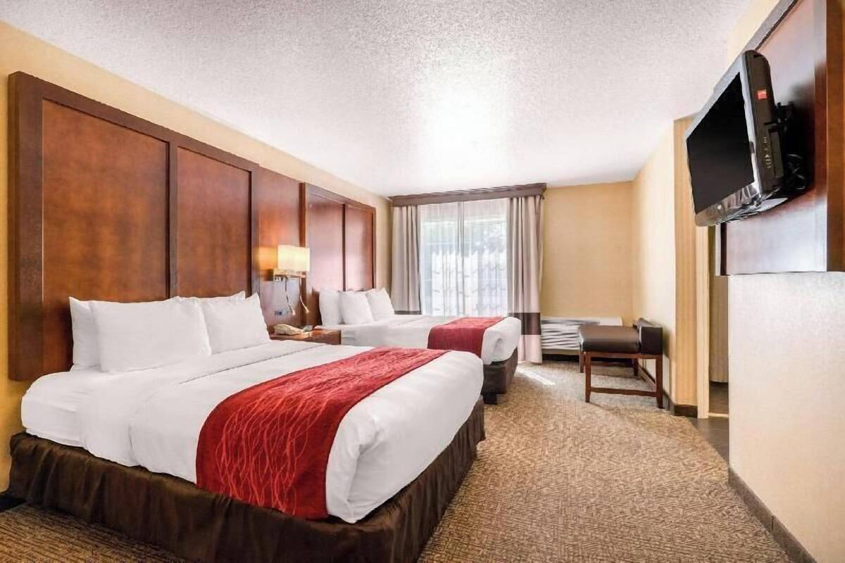 A hotel room with two beds, a desk, a television, and a window with curtains.