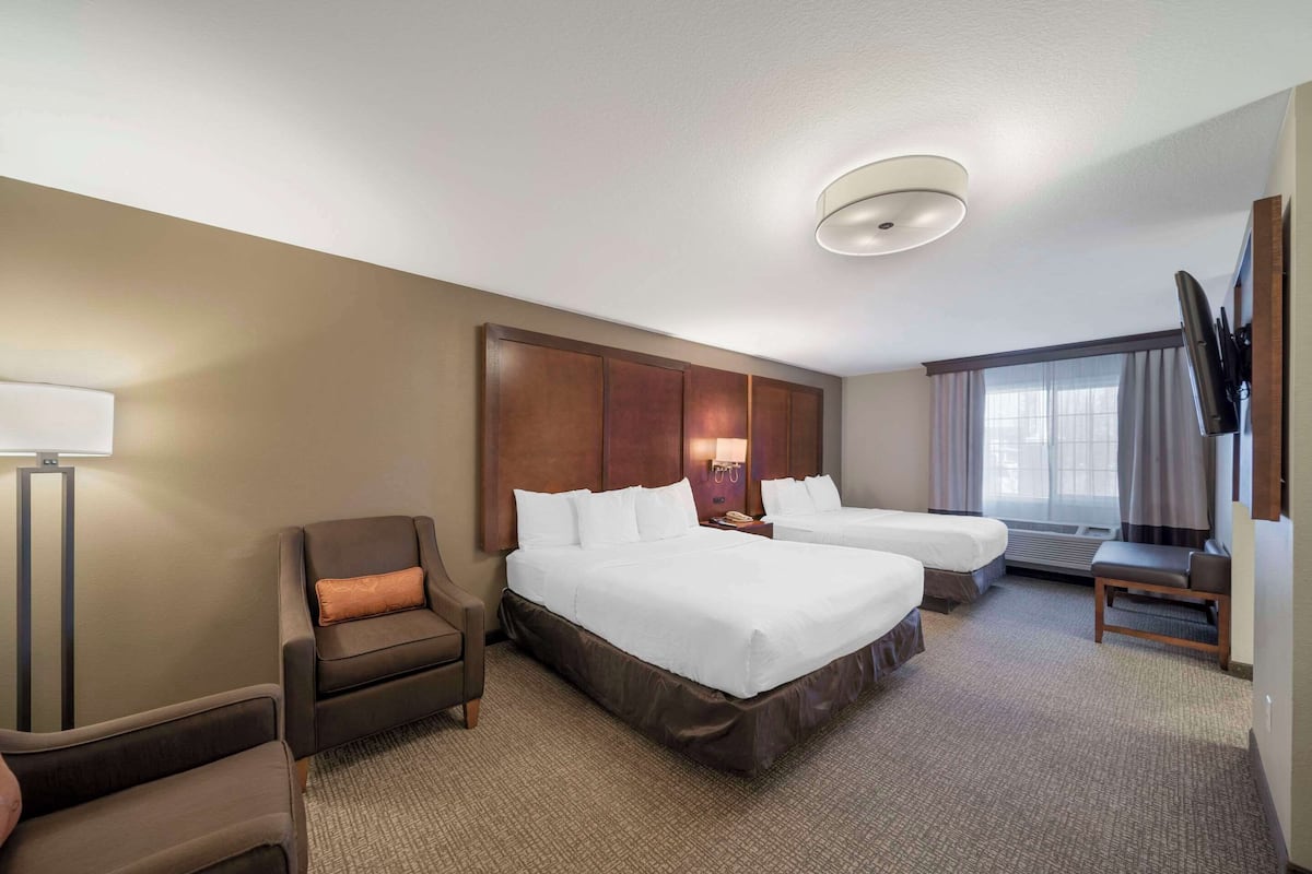 A hotel room with two beds, a desk, a chair, a flat-screen TV, and a large window with curtains.