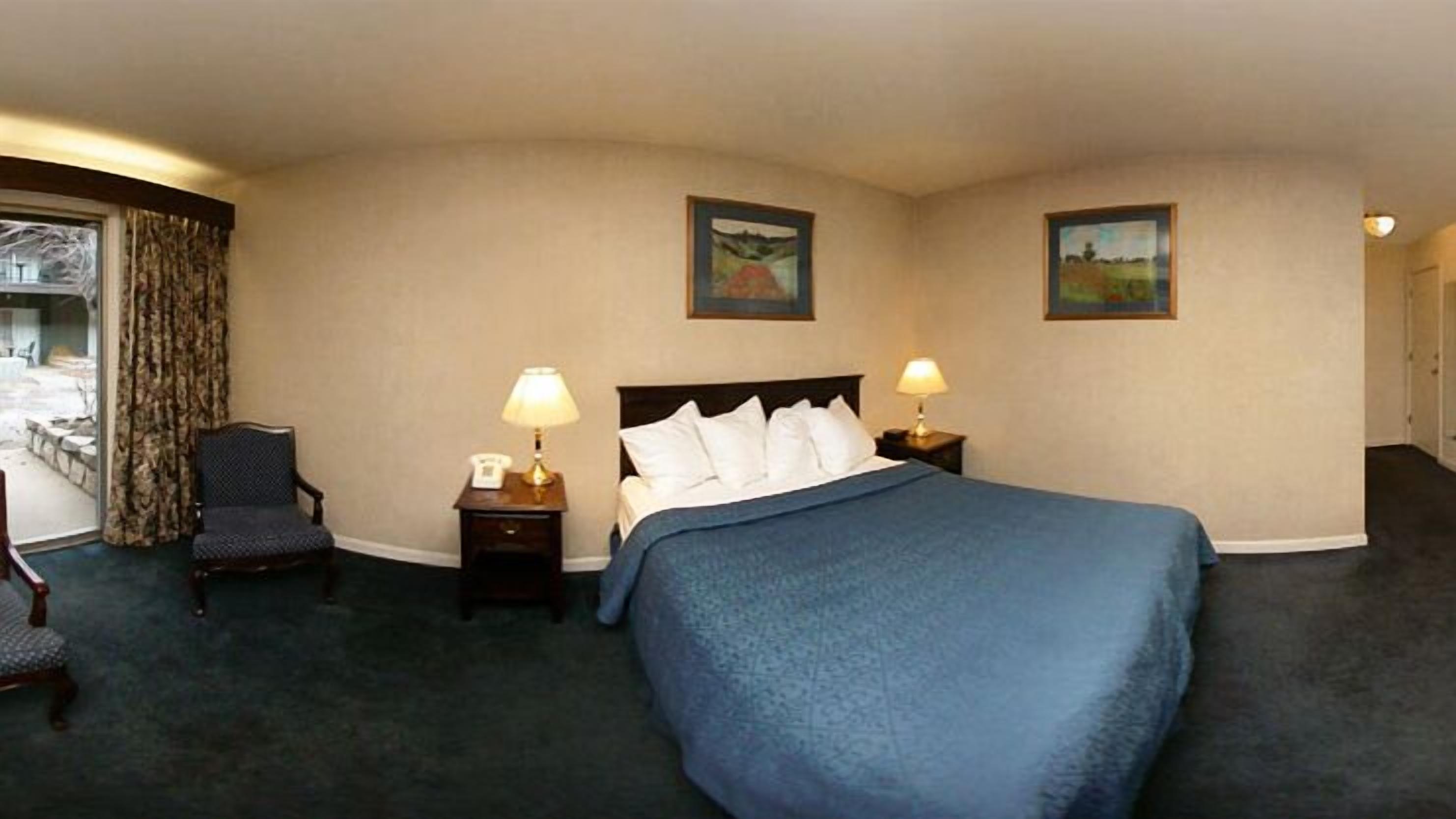 A hotel room with a large bed, two bedside tables with lamps, a chair, and two paintings on the walls.