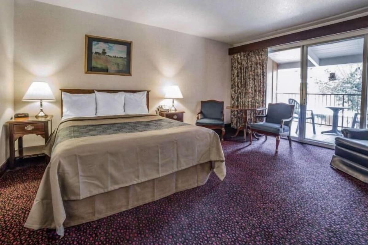 Una habitación de hotel con una cama, dos mesitas de noche con lámparas, una silla, una mesa y un balcón con sillas.