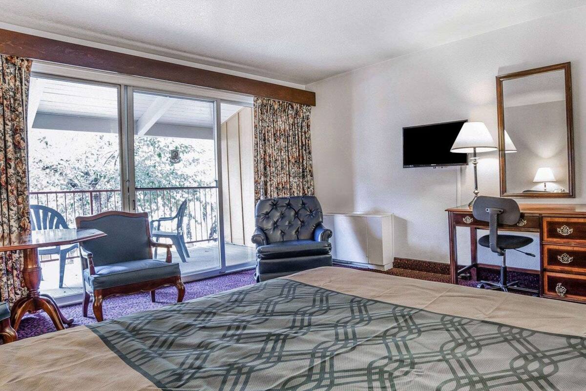 A hotel room with a bed, a desk with a chair, a television, and a balcony with chairs.