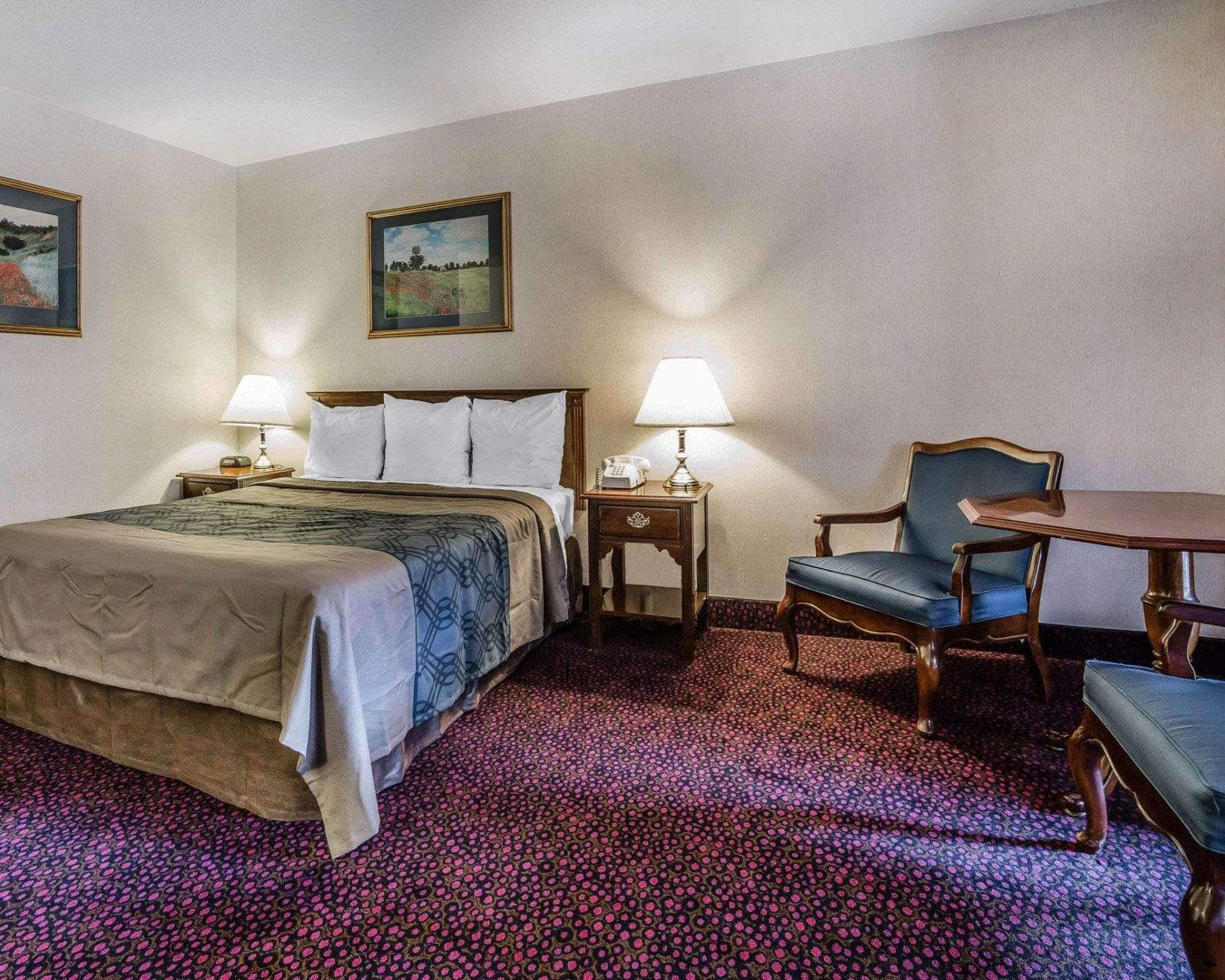 Una habitación de hotel con una cama grande, dos mesitas de noche con lámparas, una silla y una pequeña mesa.