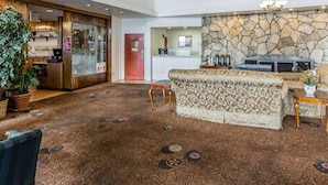 Un hall d’entrée spacieux, doté d’un tapis à motifs, d’un comptoir de réception, d’un mur en pierre et d’un coin salon avec un canapé à motifs.