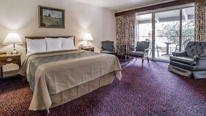 Une chambre d’hôtel avec un grand lit, deux tables de chevet avec des lampes, un fauteuil, un canapé et un balcon avec vue.