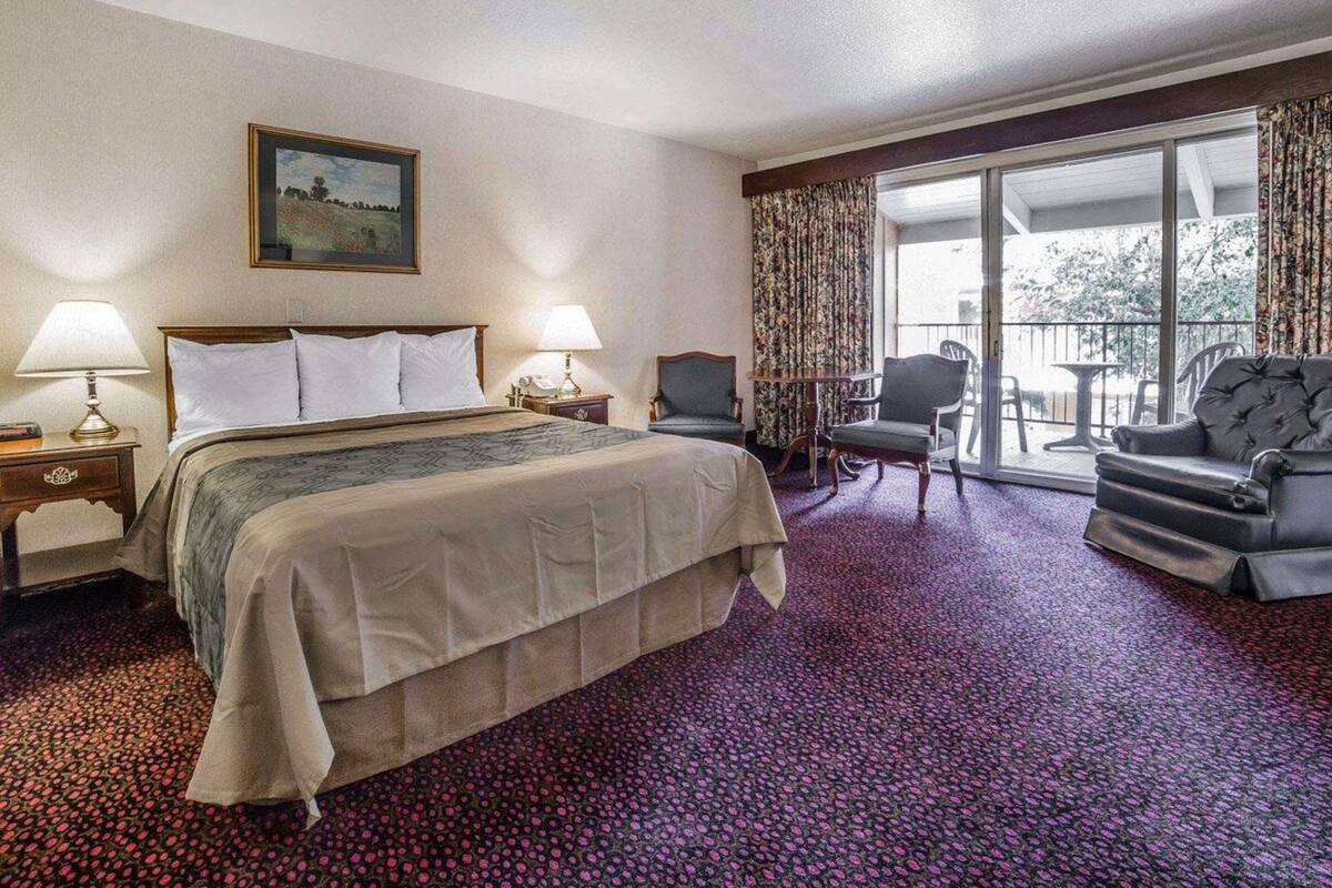 A hotel room with a large bed, two bedside tables with lamps, a chair, a sofa, and a balcony with a view.