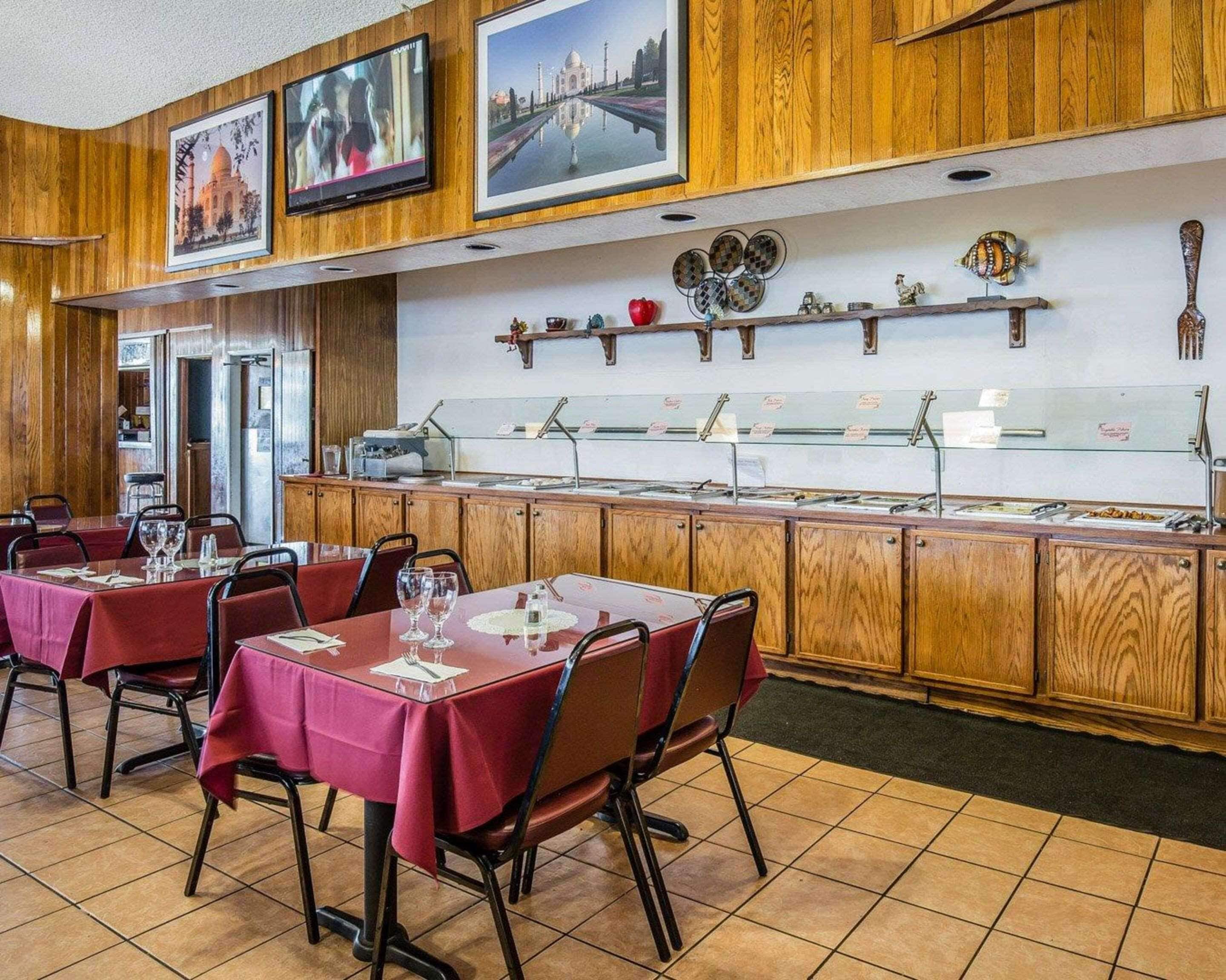 A restaurant with wooden paneling, tables with red tablecloths, and a buffet area with various food items.