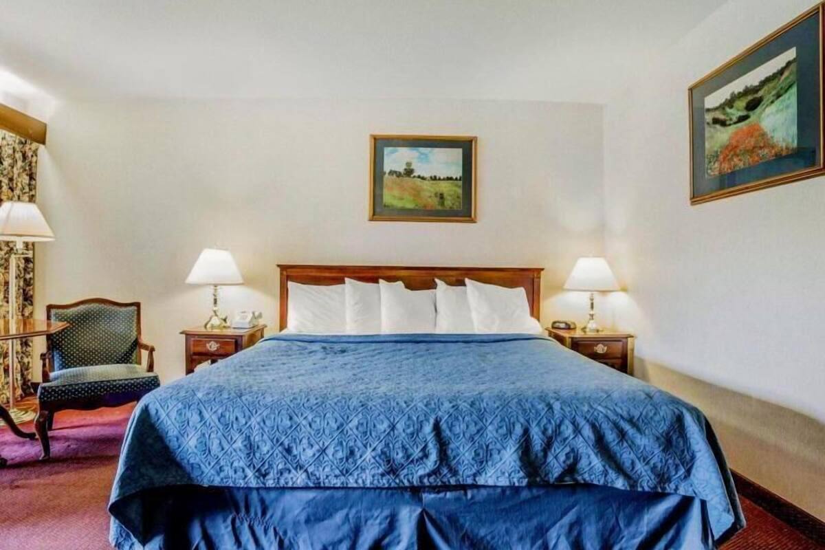 A hotel room with a large bed, two bedside tables with lamps, a chair, and a painting on the wall.
