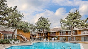 Un espace piscine avec une eau d’un bleu limpide, entouré de chaises longues et d’un bâtiment en pierre doté de balcons.