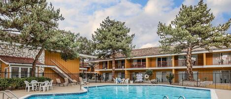 A pool area with a clear blue pool, surrounded by lounge chairs and a stone building with balconies.
