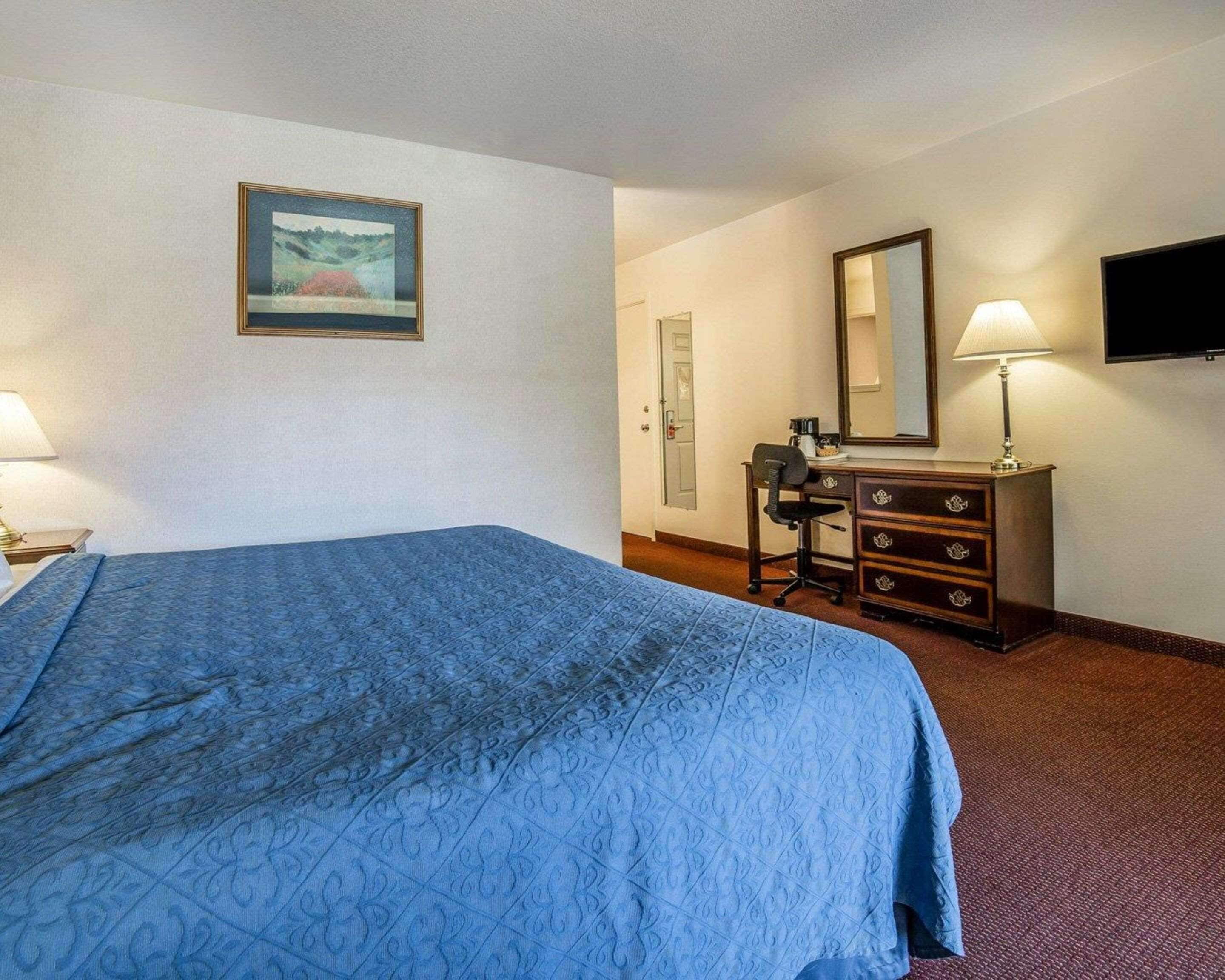 A hotel room with a bed, a dresser, a desk, a chair, a television, and a painting on the wall.