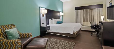 A hotel room with a bed, a desk, a chair, a couch, and a television.