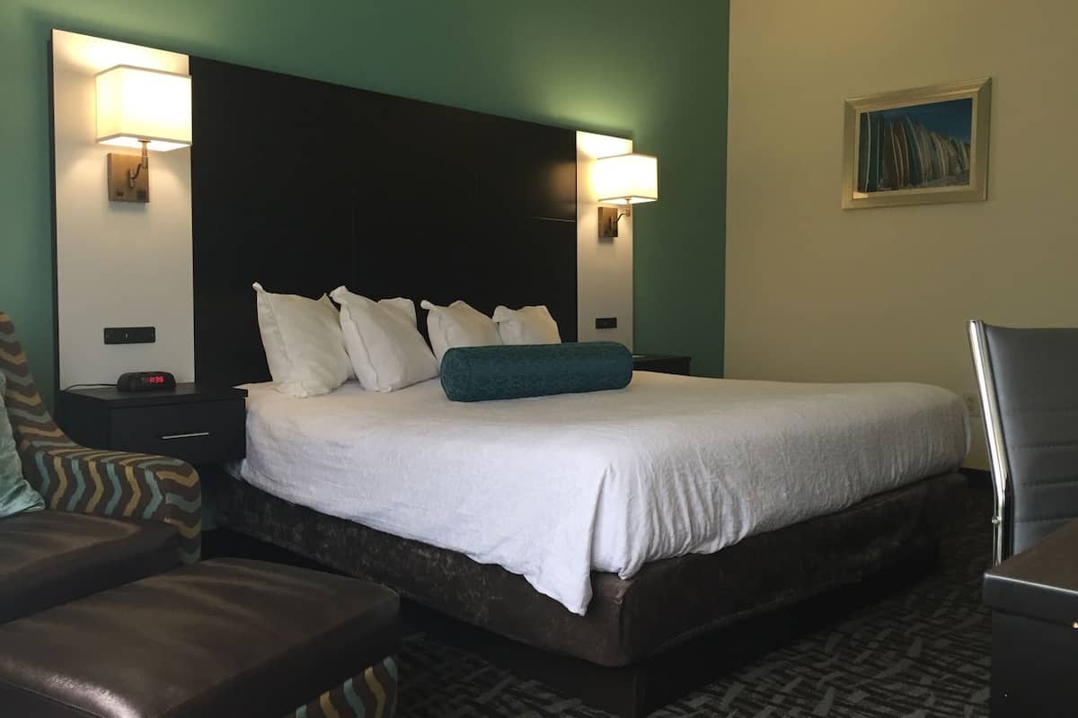 Una habitación de hotel con una cama, dos mesitas de noche, una silla, un reloj y un cuadro en la pared.