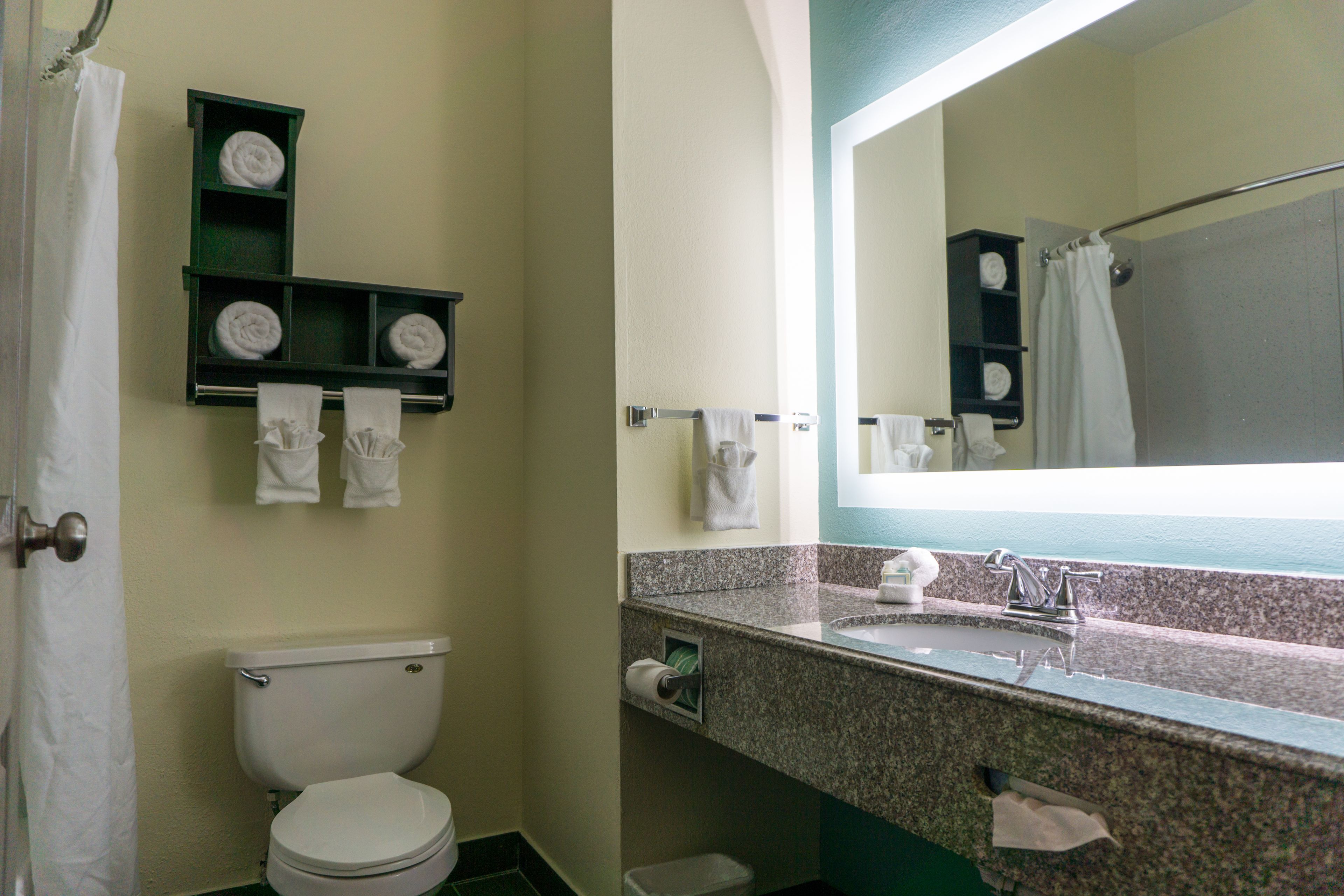 A bathroom with a toilet, a sink, and a mirror. There are shelves with towels and a shower curtain.