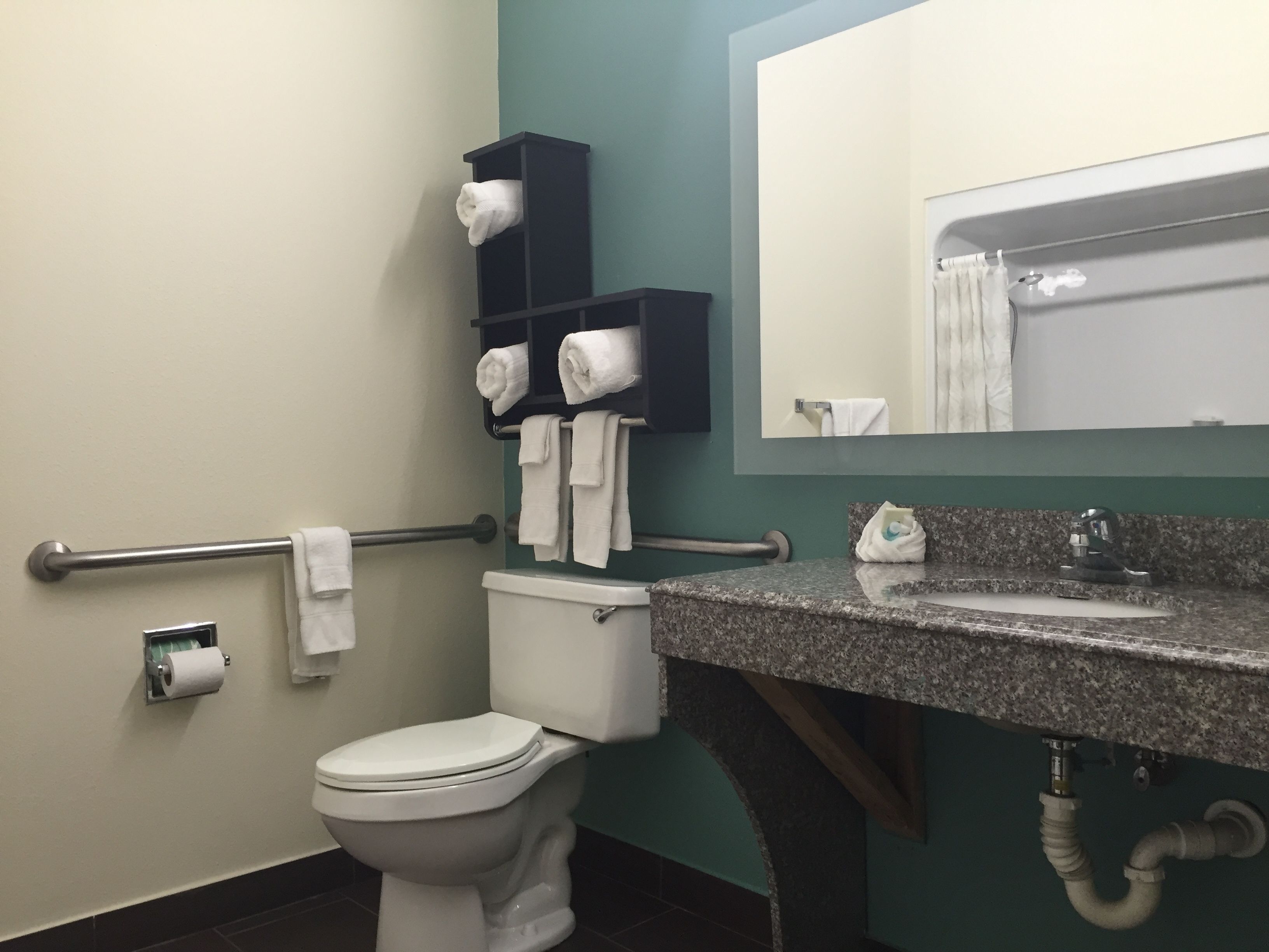 A bathroom with a toilet, a sink with a granite countertop, a towel rack with multiple towels, and a mirror above the sink.