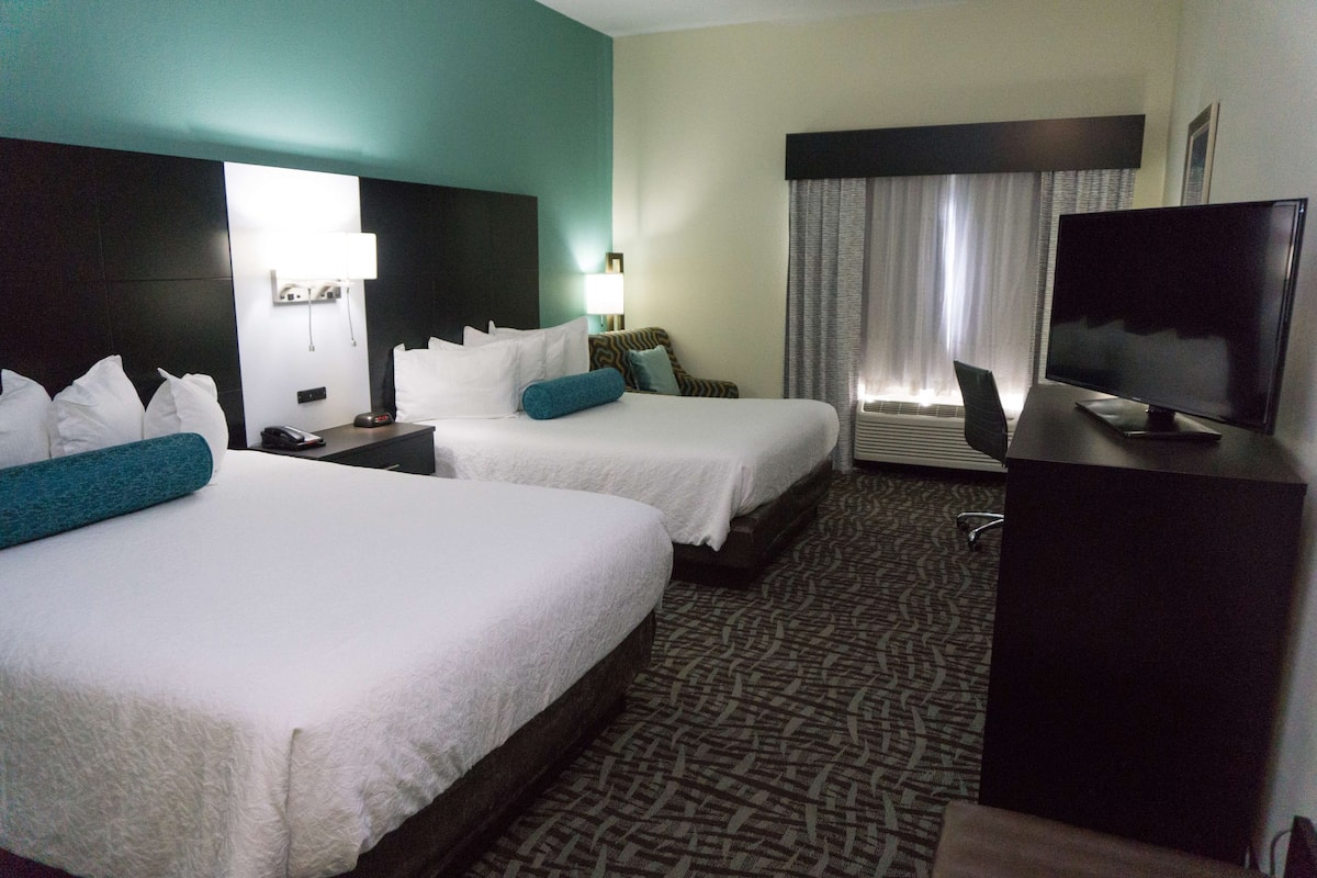 Habitación de hotel con dos camas, televisión, escritorio y ventana con cortinas.