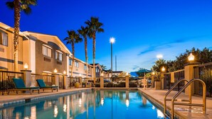 A swimming pool with lounge chairs and palm trees, surrounded by buildings with large windows and a clear sky. - Best Western Mayport Inn & Suites (Atlantic Beach)