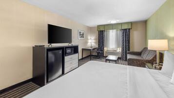 Une chambre d’hôtel dotée d’un grand lit, d’un bureau avec un ordinateur, d’une télévision et d’un coin salon comprenant une chaise et un canapé.