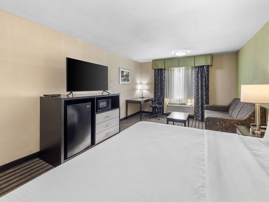 Une chambre d’hôtel dotée d’un grand lit, d’un bureau avec un ordinateur, d’une télévision et d’un coin salon comprenant une chaise et un canapé.
