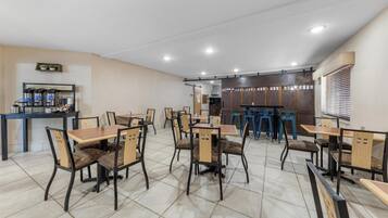 A spacious dining area with multiple tables and chairs, a coffee station, and a kitchen area in the background.