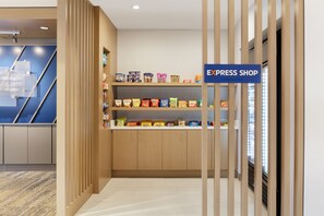 A hotel lobby with a reception desk, a blue sign reading "EXPRESS SHOP," and shelves stocked with snacks.