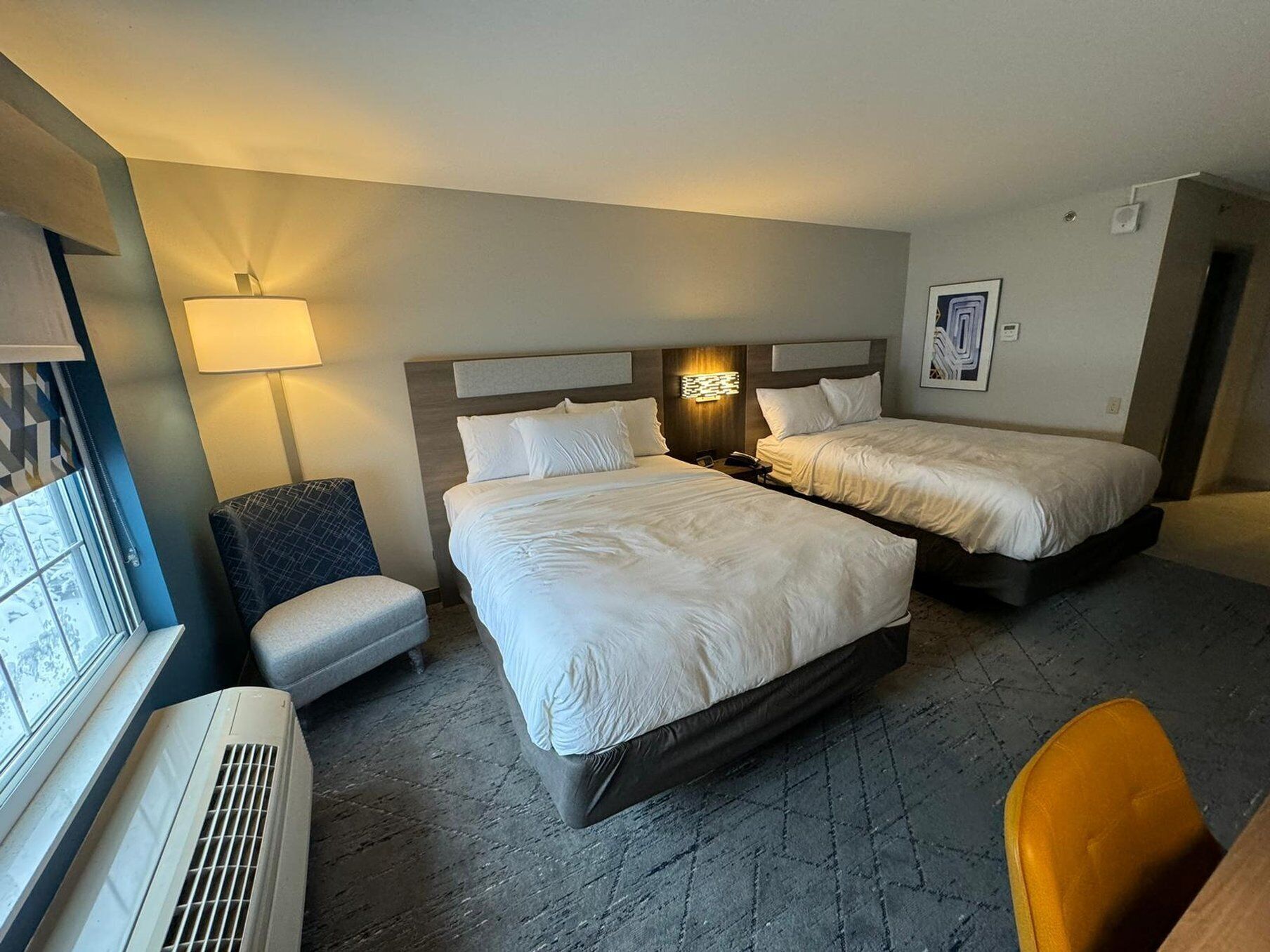 Ein Hotelzimmer mit zwei Betten, einem Schreibtisch, einem Stuhl, einer Lampe und einem Fenster.