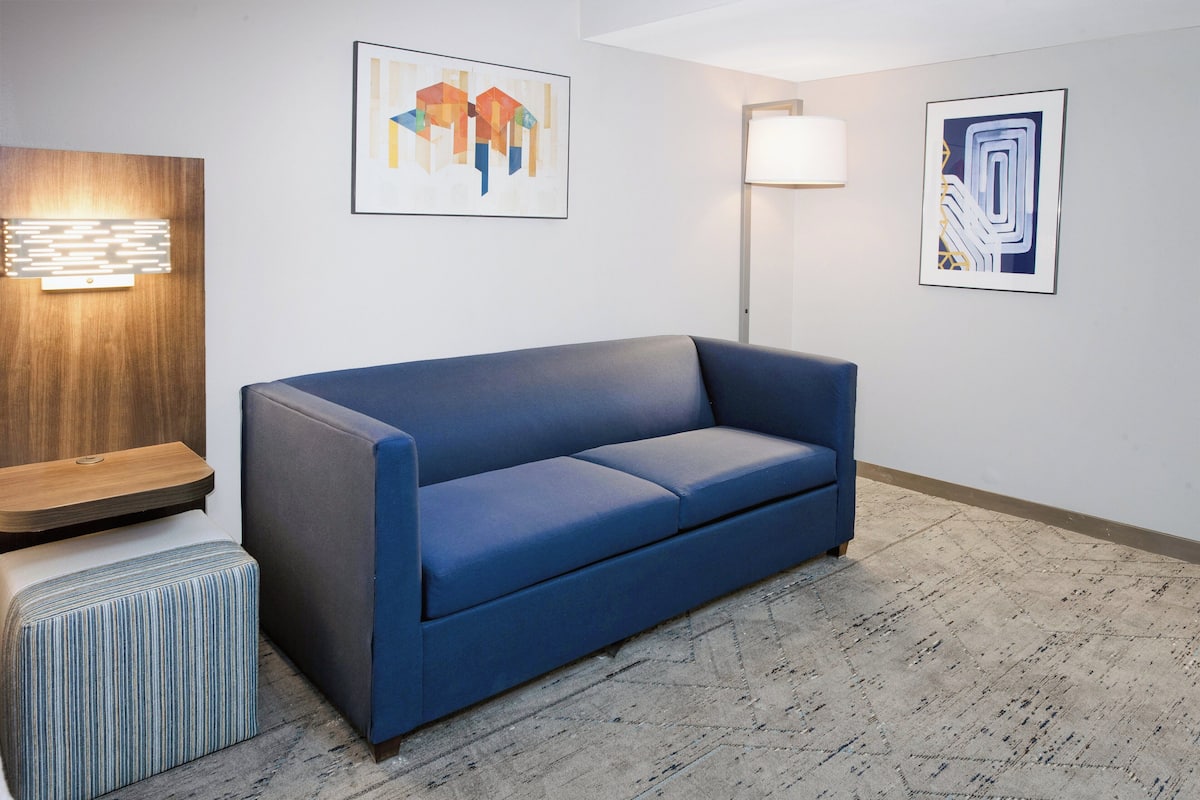 A modern room with a blue sofa, a striped ottoman, a wooden accent wall, and abstract art on the walls.