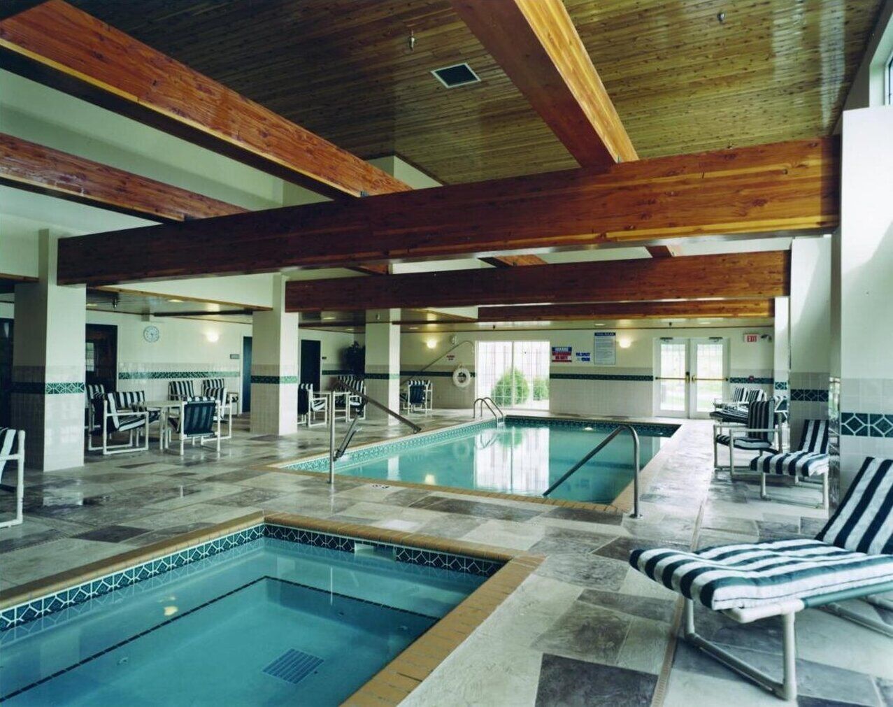 An indoor swimming pool with multiple lanes, lounge chairs, and a wooden ceiling structure.