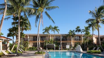 A hotel with a swimming pool, palm trees, and lounge chairs.